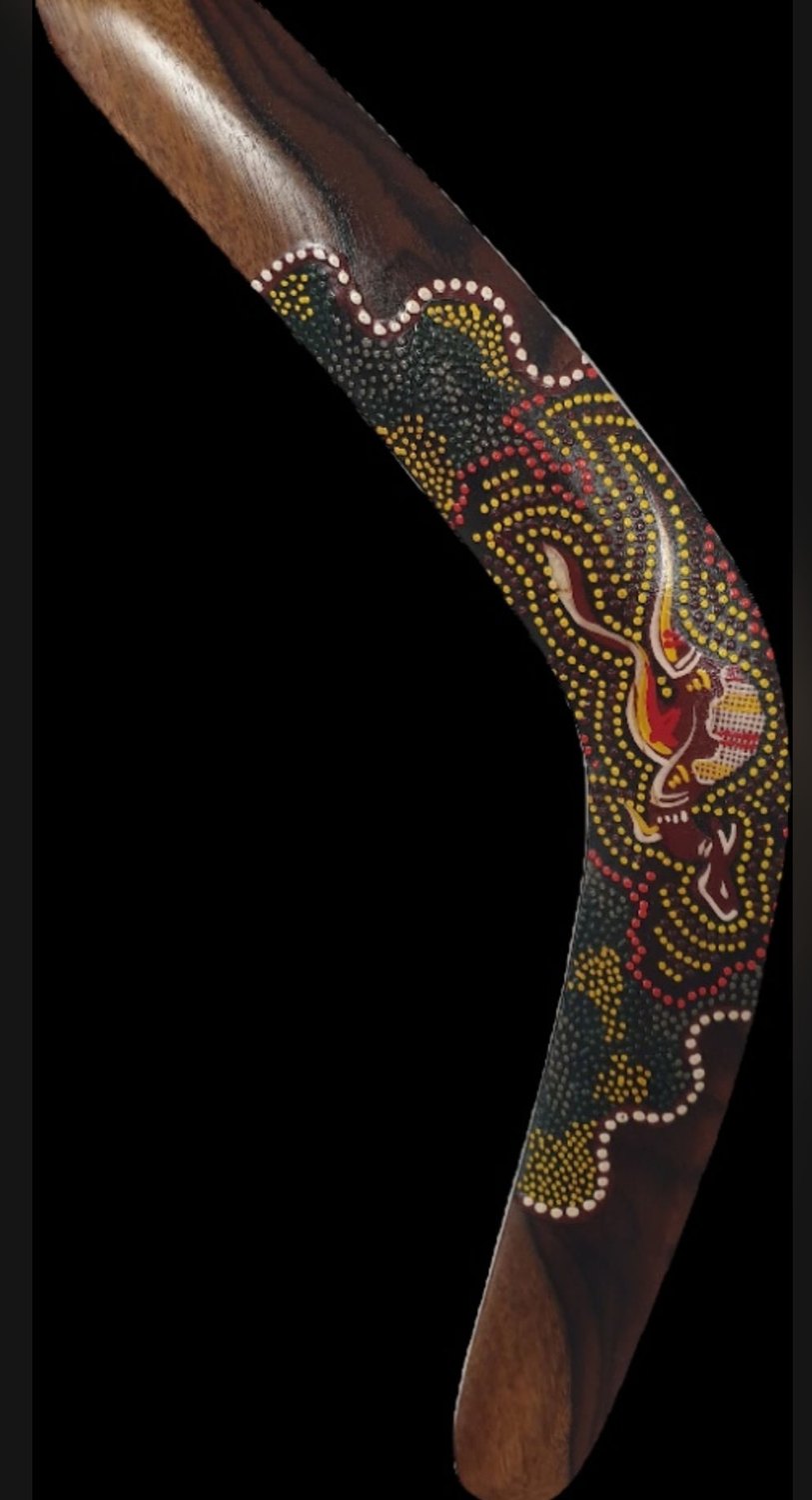 A dark contemporary boomerang densely dot-painted in yellow, red and white around a central fire-lizard figure / Un bumerang contemporan închis la culoare, pictat dens cu puncte galbene, roșii și albe în jurul unei figuri centrale de șopârlă-foc