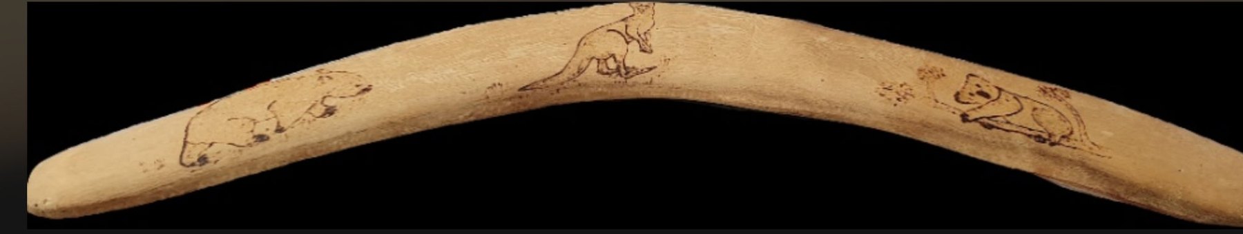A pale-wood souvenir boomerang decorated in pyrography with a wombat, a kangaroo and a koala / Un bumerang-suvenir din lemn deschis la culoare, decorat în pirogravură cu un wombat, un cangur și un koala