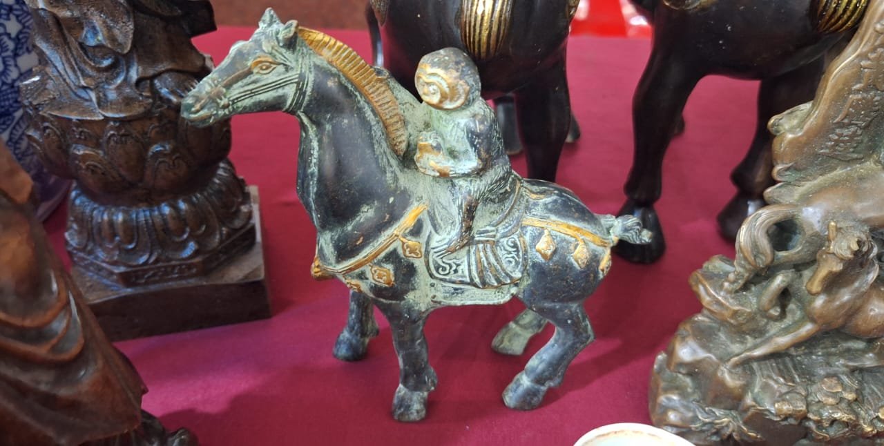 The bronze monkey-on-horseback figurine on a market table among other carved figures